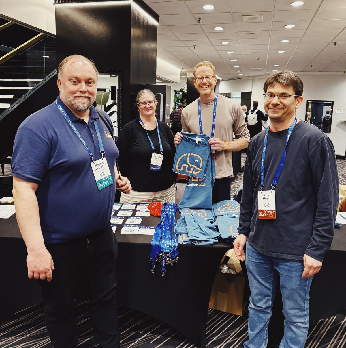 Magnus Hagander, Katherine Saar, Paul Ramsey, and Steve Singer smiling beside the registration desk