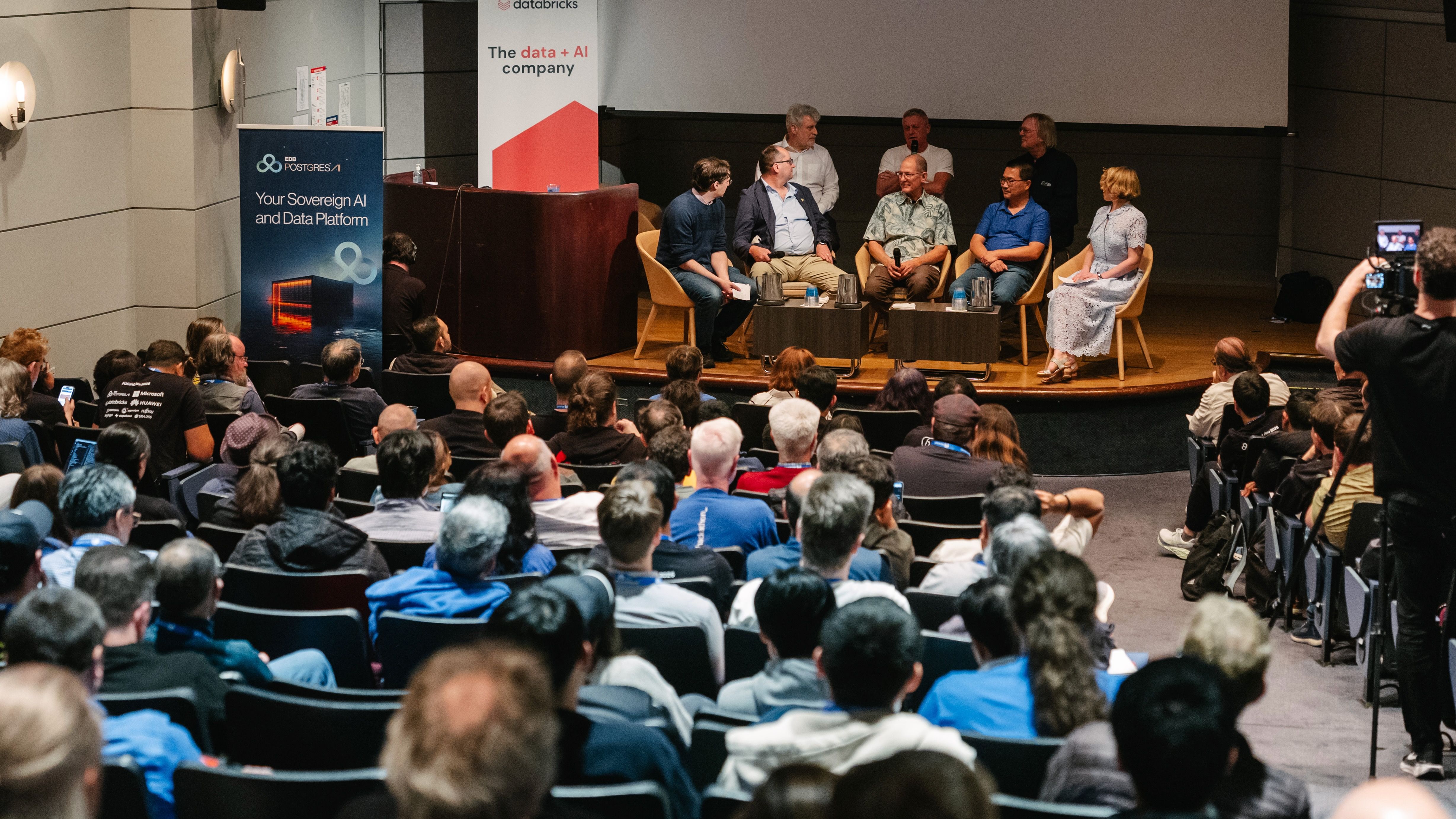 A packed auditorium, nearly every seat taken, facing a panel of eight seated on stage